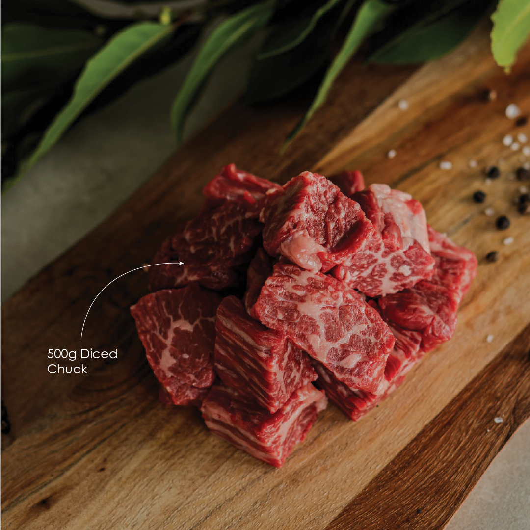 Diced beef on a wooden cutting board with green leaves and peppercorns.