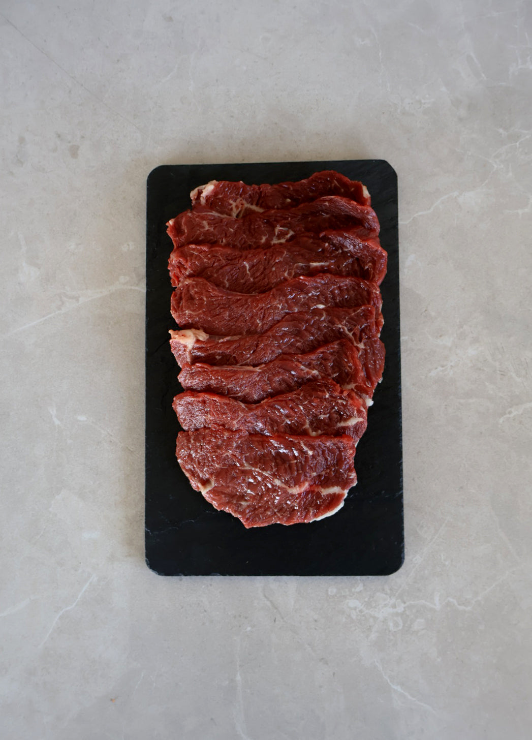 Raw beef wagyu yakiniku slices on a black stone surface with a light gray background