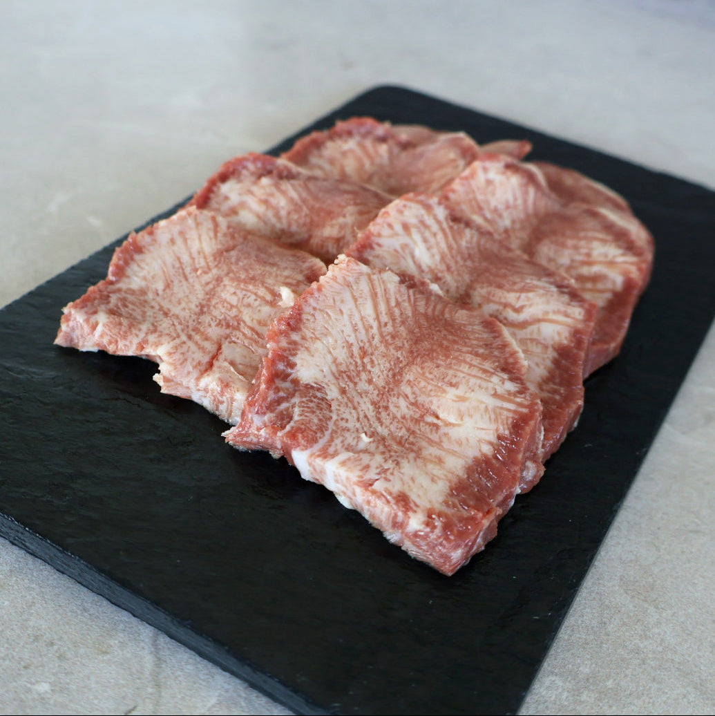 Raw wagyu tongue Yakiniku slices on a black slate board with a light background