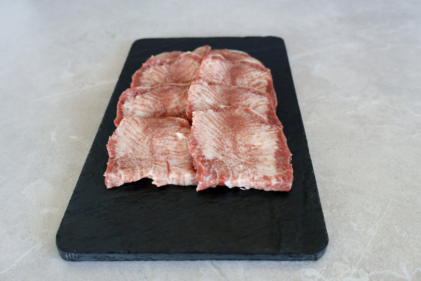 Wagyu beef tongue on a black cutting board with a light gray background