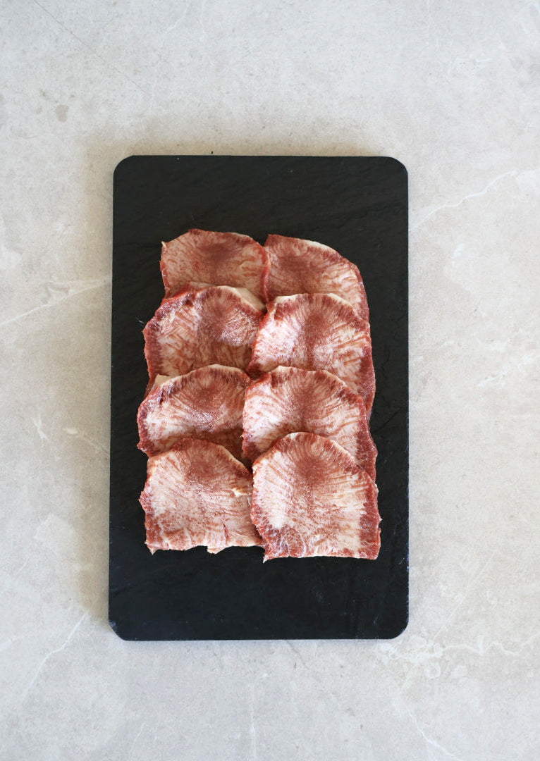 Sliced raw wagyu tongue meat on a black cutting board with a light gray background