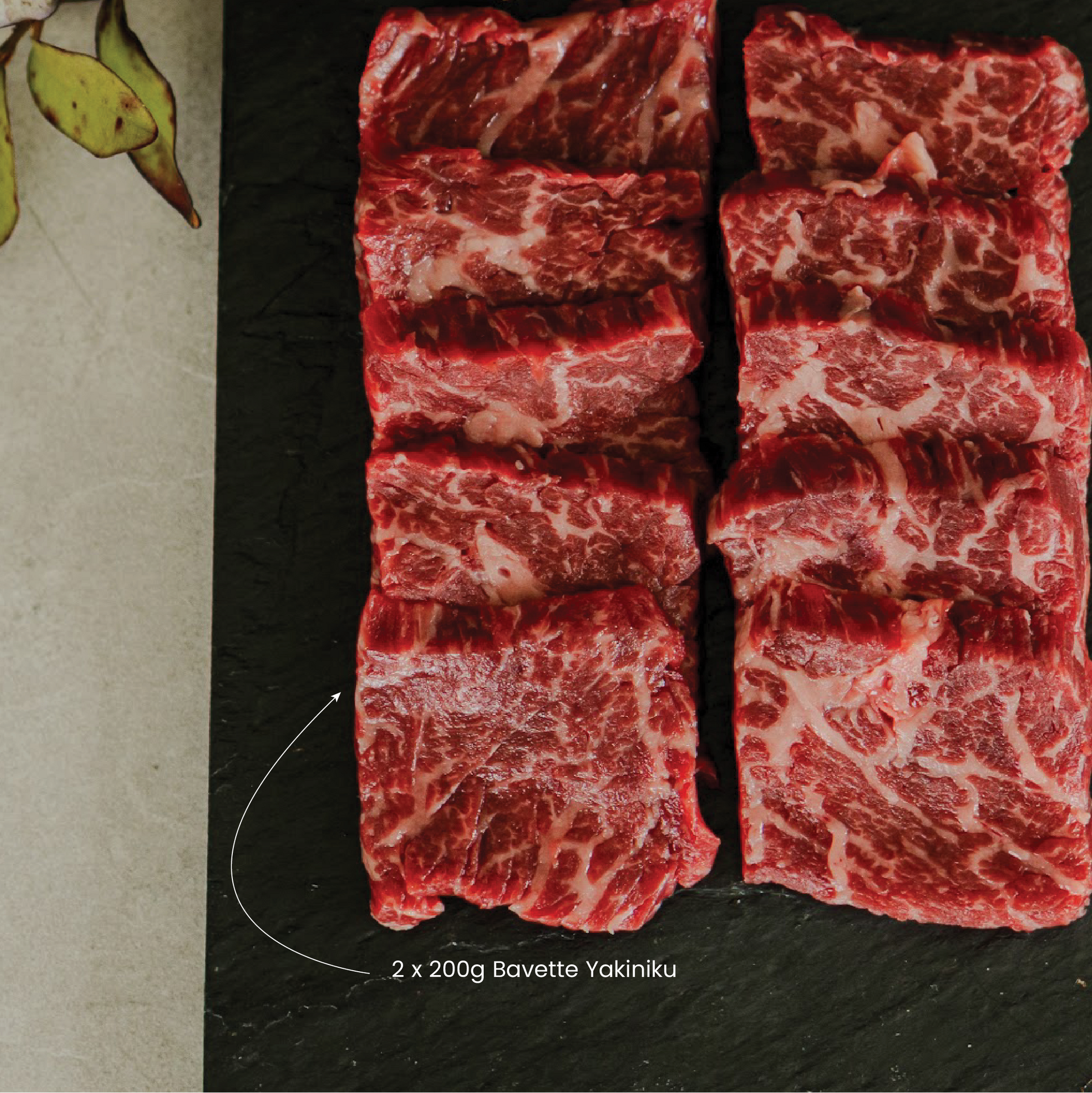 Raw bavette yakiniku Wagyu beef slices on a black slate surface with green leaves.