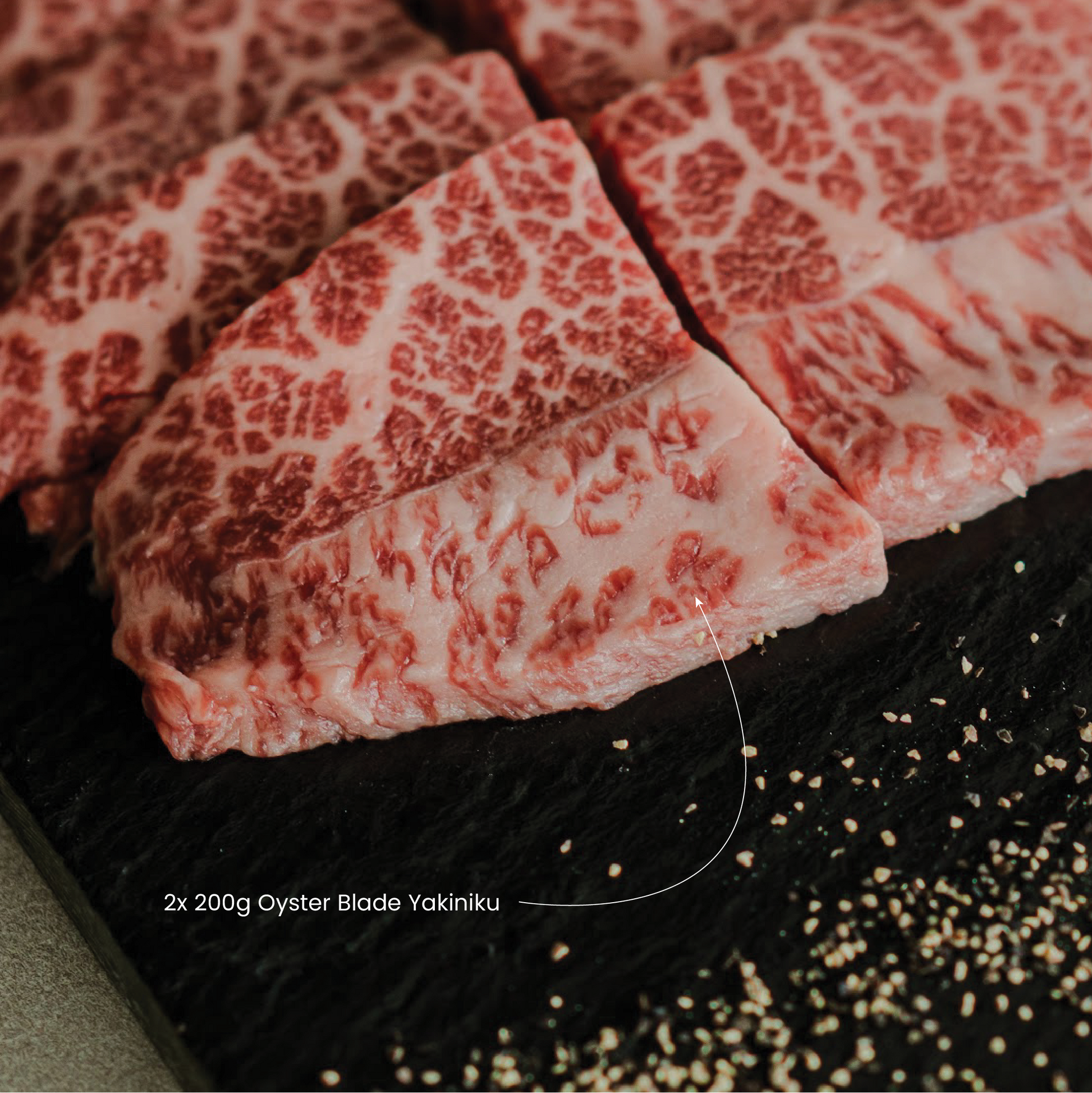 Raw marbled ouster blade meat slices on a black surface with sesame seeds.