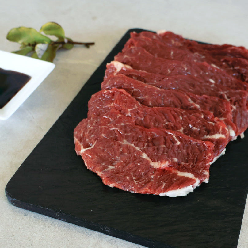 Raw wagyu beef rump on a black cutting board with a white background