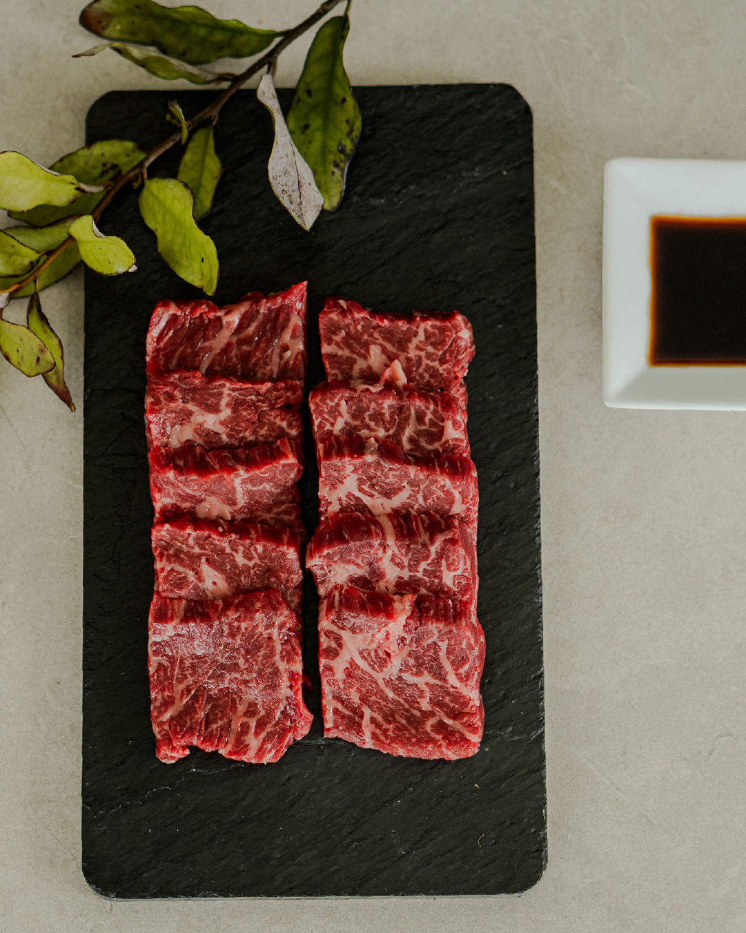 Raw beef slices on a black slate board with a side of soy sauce.