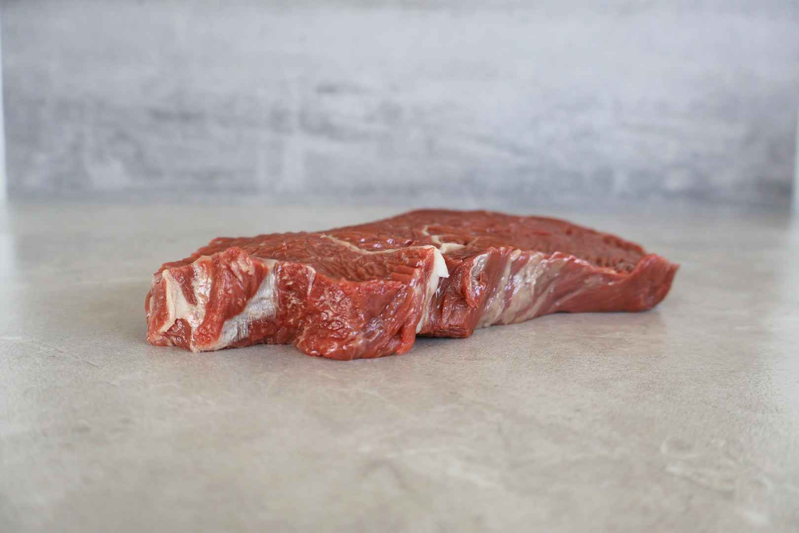 Raw Wagyu rump steak on a light gray surface with a neutral background