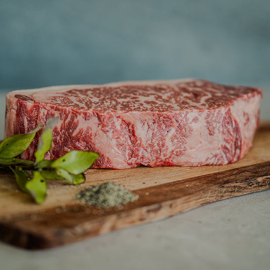 Black Origin Wagyu raw sirloin steak on a wooden board with horopito herb garnish